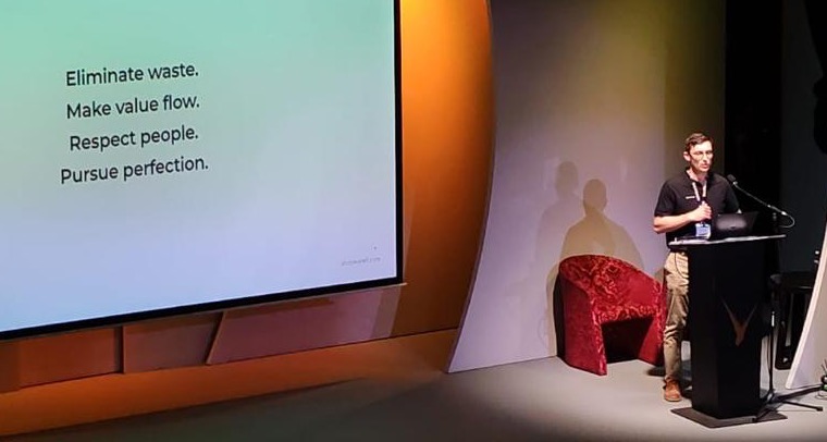 Gerhard Bekker speaking at a podium at the Lean Conference, Melrose Arch, 28 August 2026. The slide behind him reads: Eliminate waste. Make value flow. Respect people. Pursue perfection.